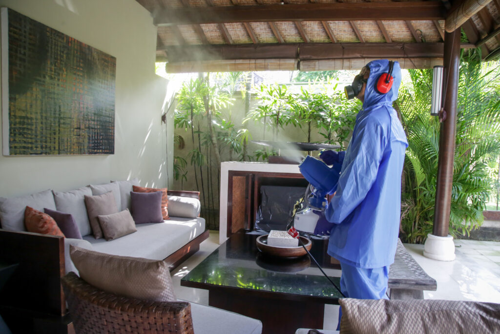 professional disinfection services worker using blue suit desinfecting living room