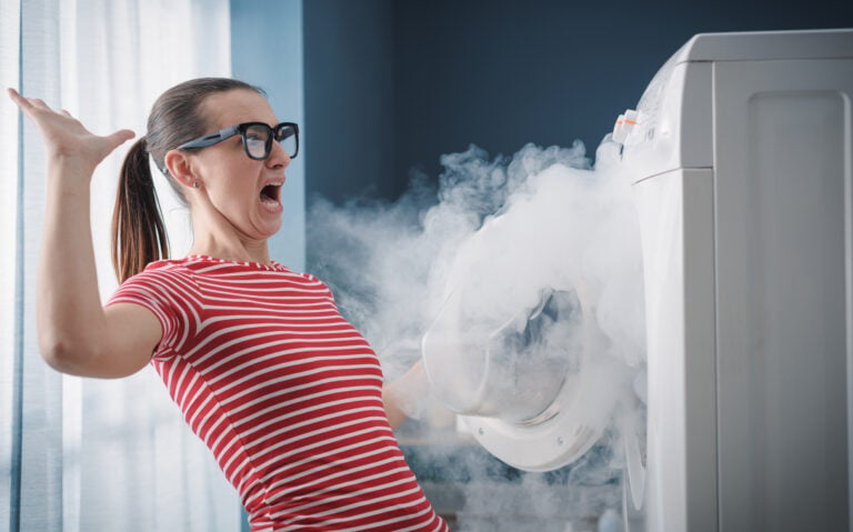 signs your dryer is going to catch fire Scared woman dealing with a broken burning appliance at home