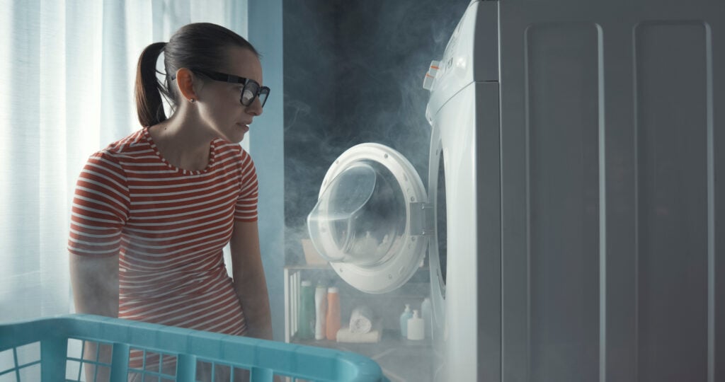 signs your dryer is going to catch fire Upset woman staring at her broken washing machine, the room is full of smoke