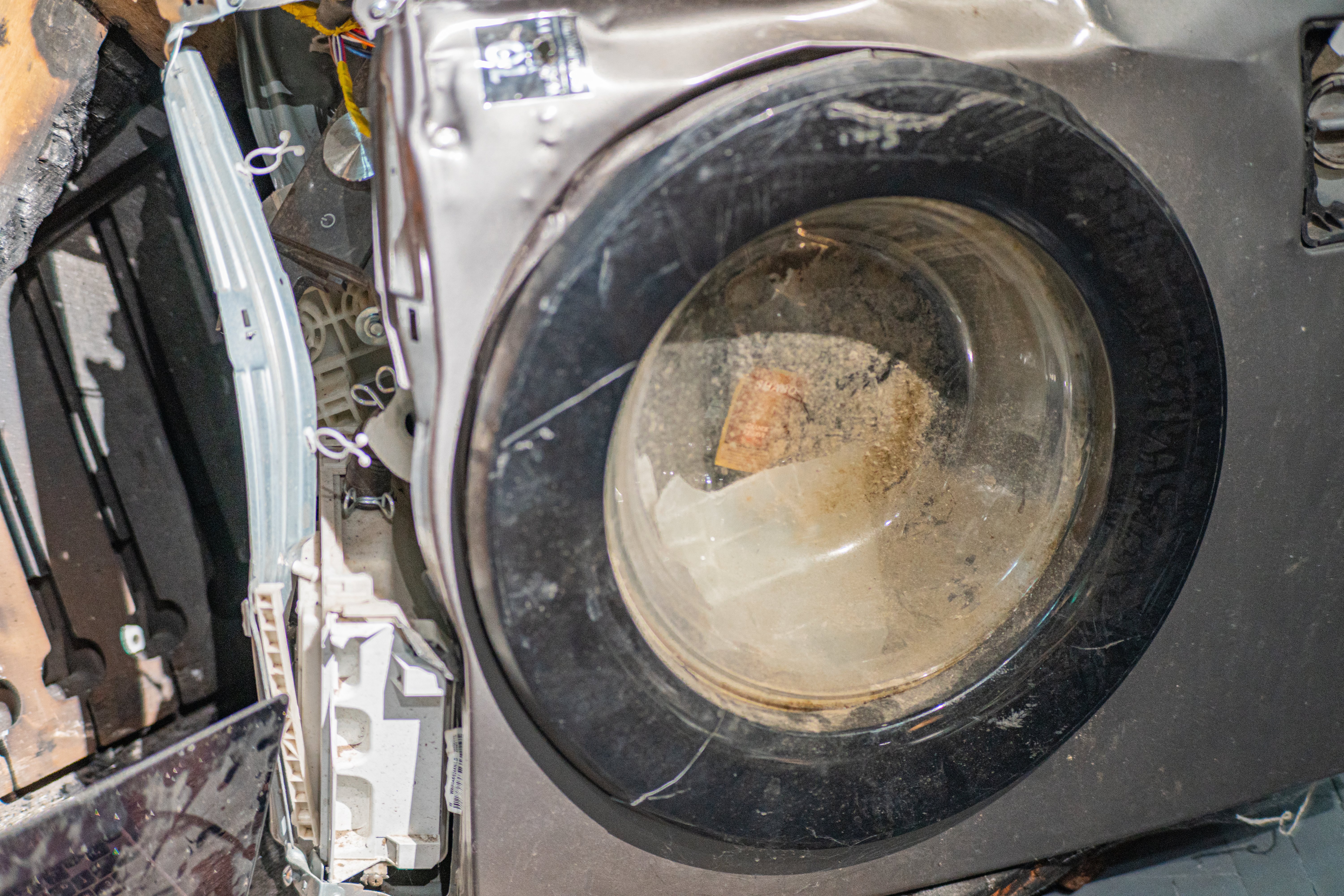 Woman checking her damaged washing machine, the floor is flooded broken washing machine after a fire in the apartment.